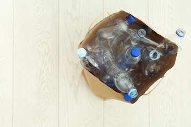 Photo of Paper bag full of used plastic bottles on floor, top view with space for text. Recycle concept