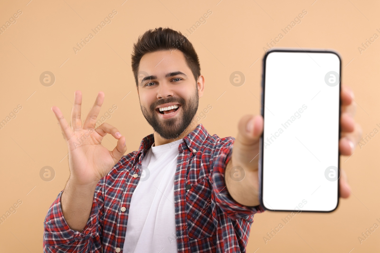 Photo of Young man showing smartphone in hand and OK gesture on beige background