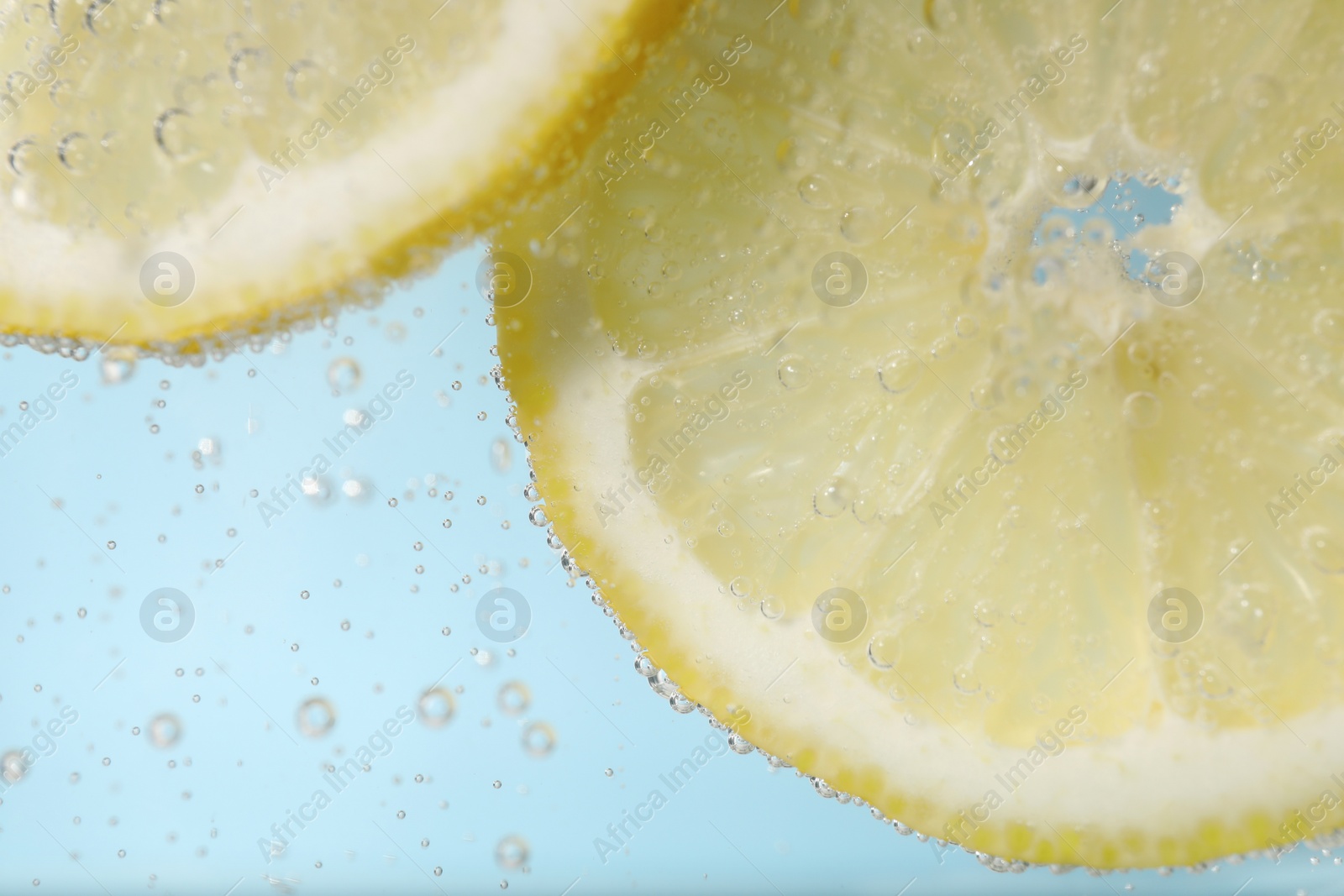 Photo of Juicy lemon slices in soda water against light blue background, closeup