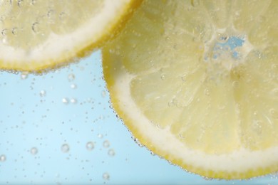 Photo of Juicy lemon slices in soda water against light blue background, closeup