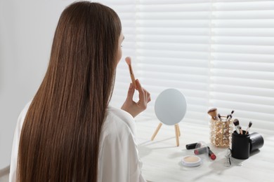 Photo of Woman applying makeup with brush at dressing table indoors. Space for text