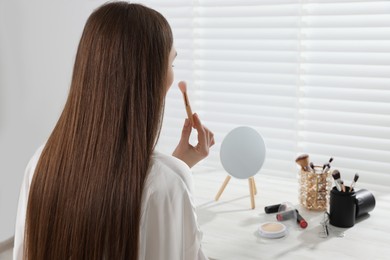 Woman applying makeup with brush at dressing table indoors. Space for text