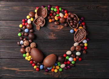 Frame made of tasty chocolate eggs and sweets on wooden table, flat lay. Space for text