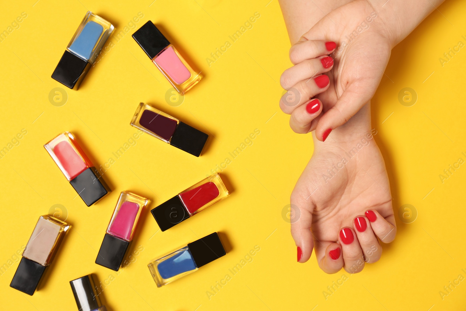 Photo of Woman with red manicure and nail polish bottles on color background, top view