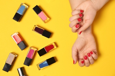 Woman with red manicure and nail polish bottles on color background, top view