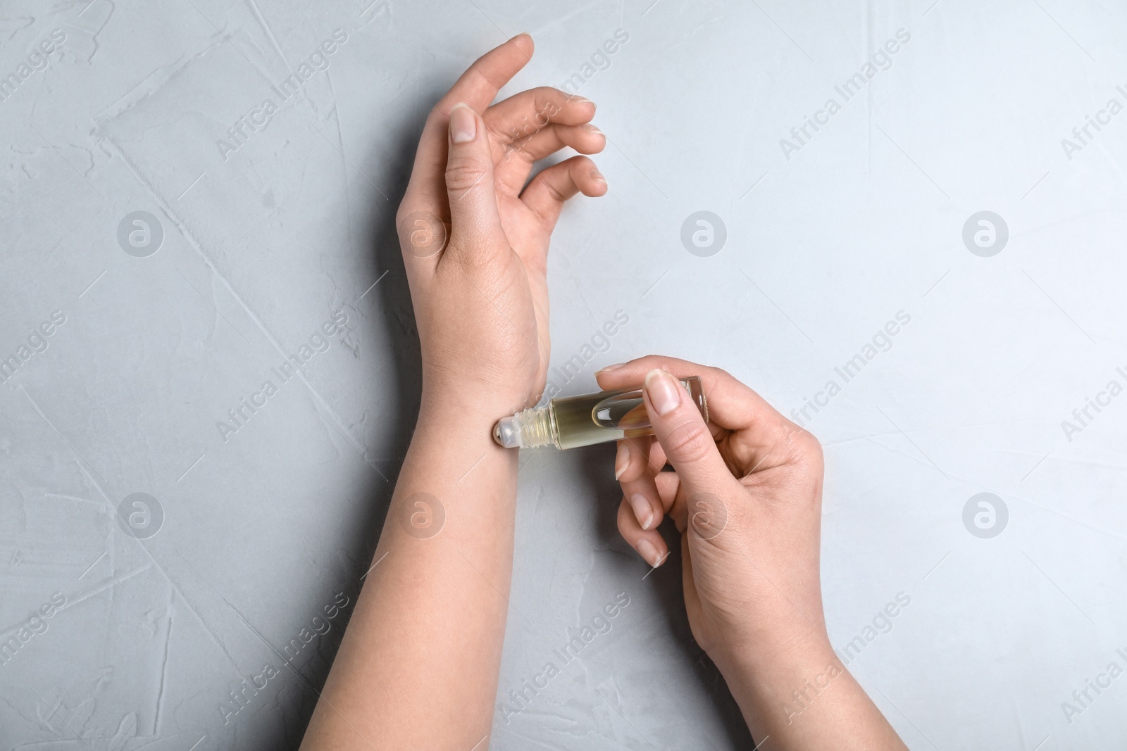 Photo of Woman applying essential oil onto her hand on light background, top view