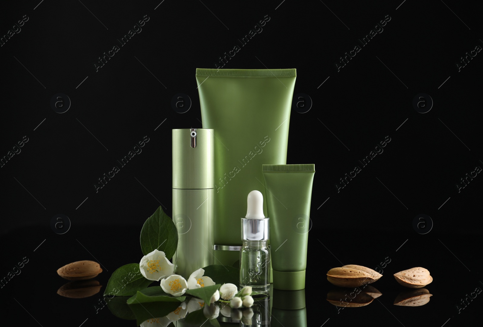 Photo of Set of cosmetic products, almond nuts and flowers on black background