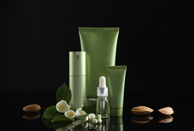 Photo of Set of cosmetic products, almond nuts and flowers on black background