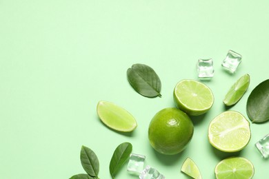Photo of Fresh ripe limes with leaves and ice cubes on light green background, flat lay