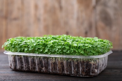 Photo of Fresh organic microgreen in plastic container on wooden table, closeup