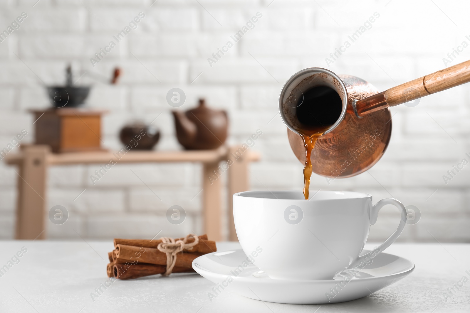 Photo of Turkish coffee. Pouring brewed beverage from cezve into cup at white table indoors