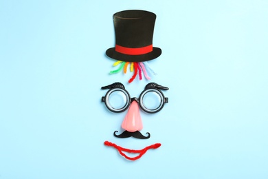 Funny face made with clown's accessories on light blue background, flat lay