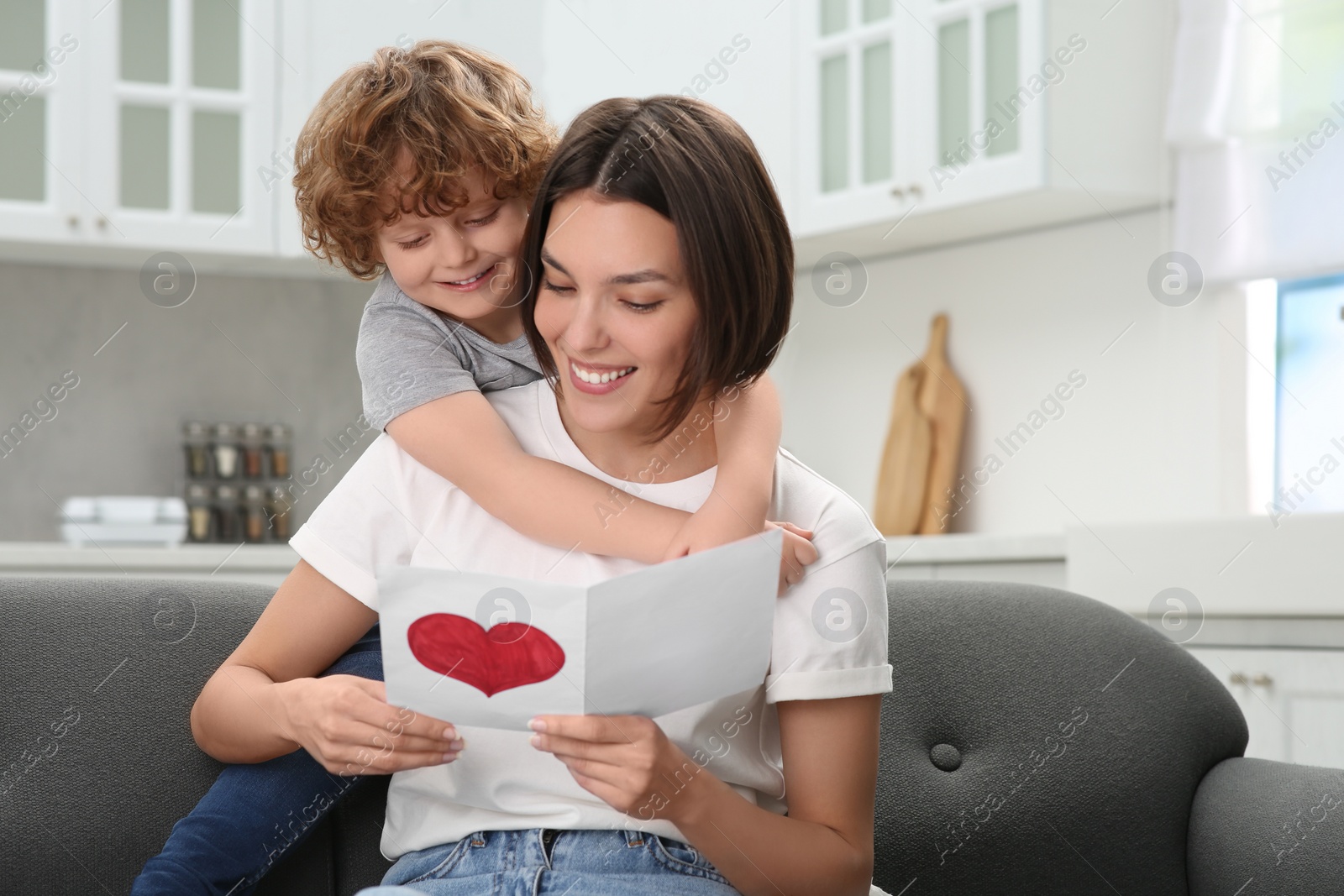 Photo of Little son congratulating his mom with Mother`s day at home. Woman holding greeting card