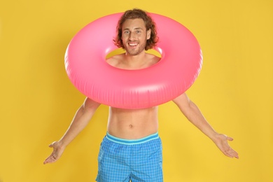 Attractive young man in beachwear with pink inflatable ring on yellow background