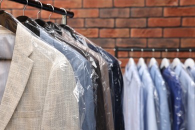 Dry-cleaning service. Many different clothes hanging on rack against brick wall, closeup