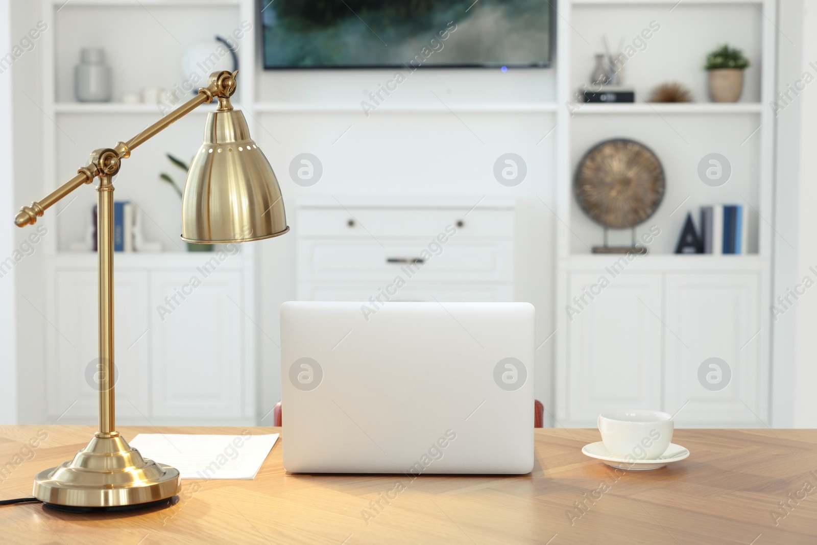 Photo of Interior design. Cosy workplace with laptop and lamp on wooden table near tv between shelves