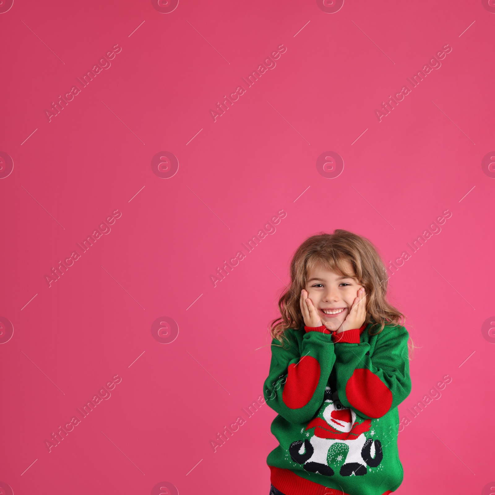 Photo of Cute little girl in green Christmas sweater smiling against pink background. Space for text