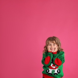 Photo of Cute little girl in green Christmas sweater smiling against pink background. Space for text