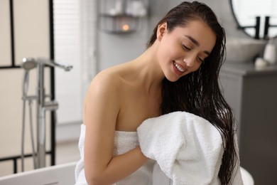 Photo of Smiling woman drying hair with towel after shower in bathroom