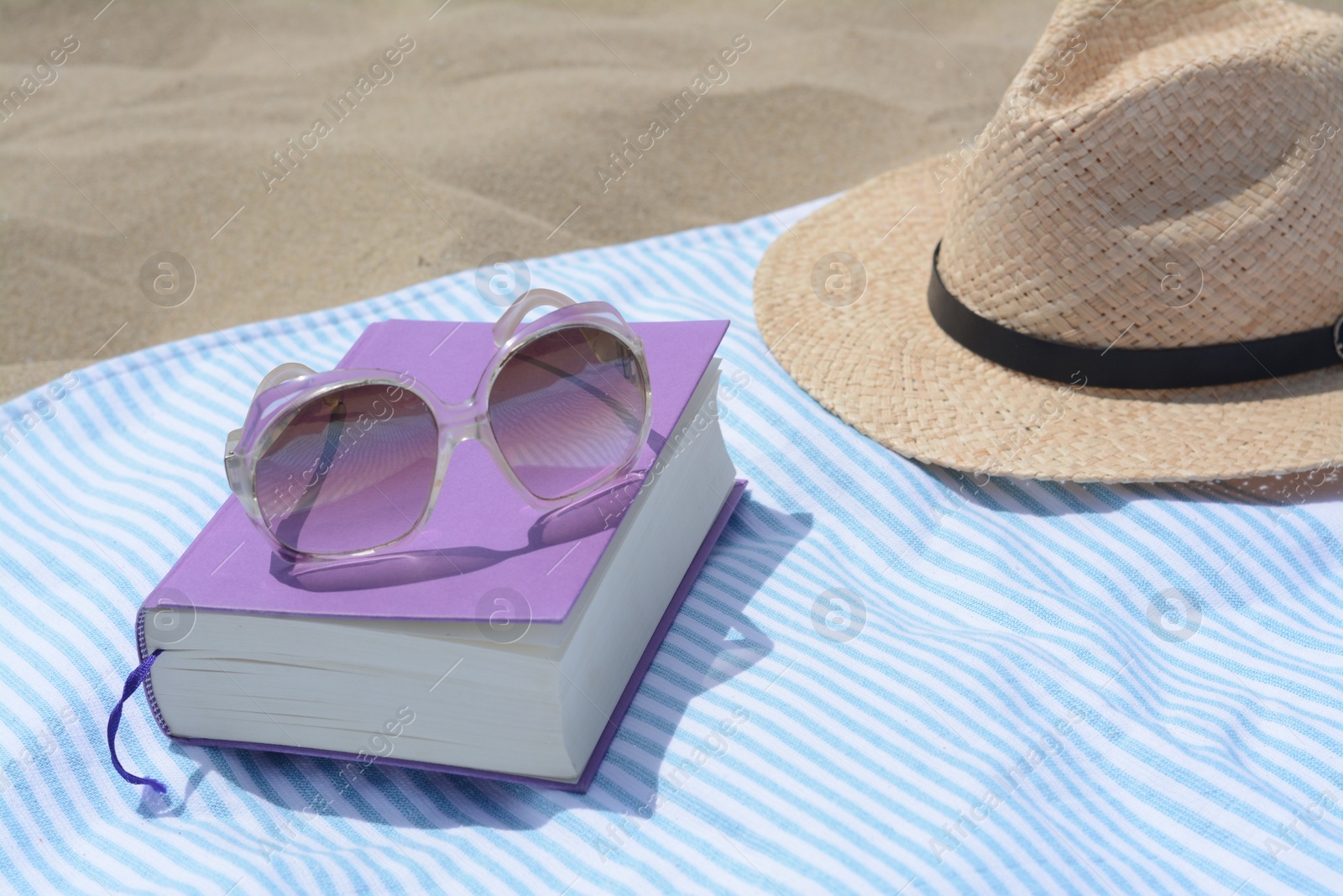 Photo of Beach towel with book, sunglasses and straw hat on sand