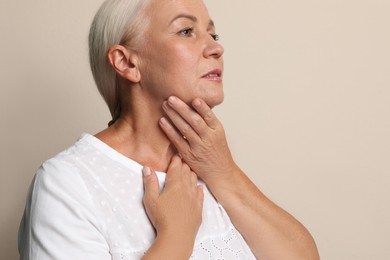 Photo of Mature woman doing thyroid self examination on beige background