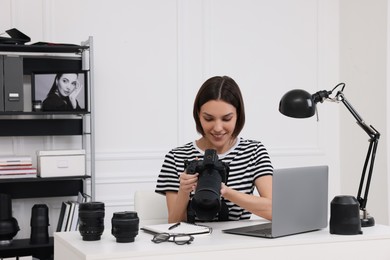 Young professional photographer with camera at table in modern photo studio