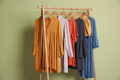 Photo of Collection of trendy women's garments on rack near green wall. Clothing rental service