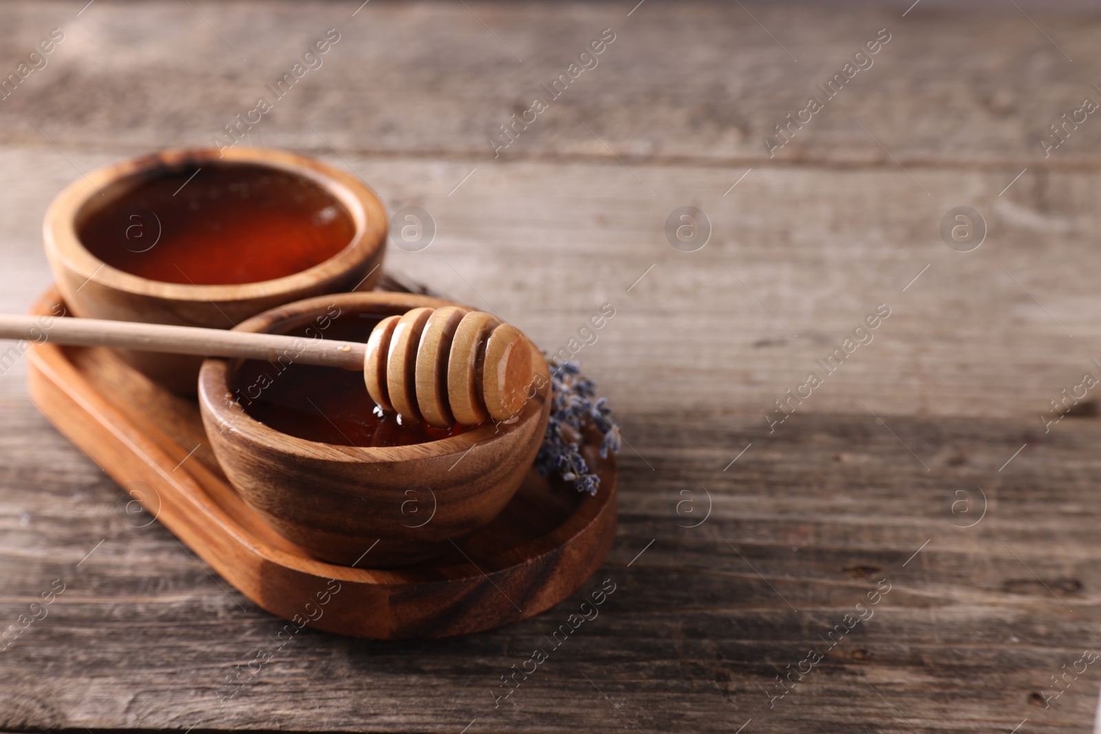 Photo of Delicious honey in bowls, lavender flowers and dipper on wooden table. Space for text