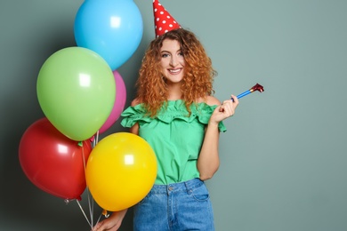 Young woman with party blower and bright balloons on color background. Birthday celebration