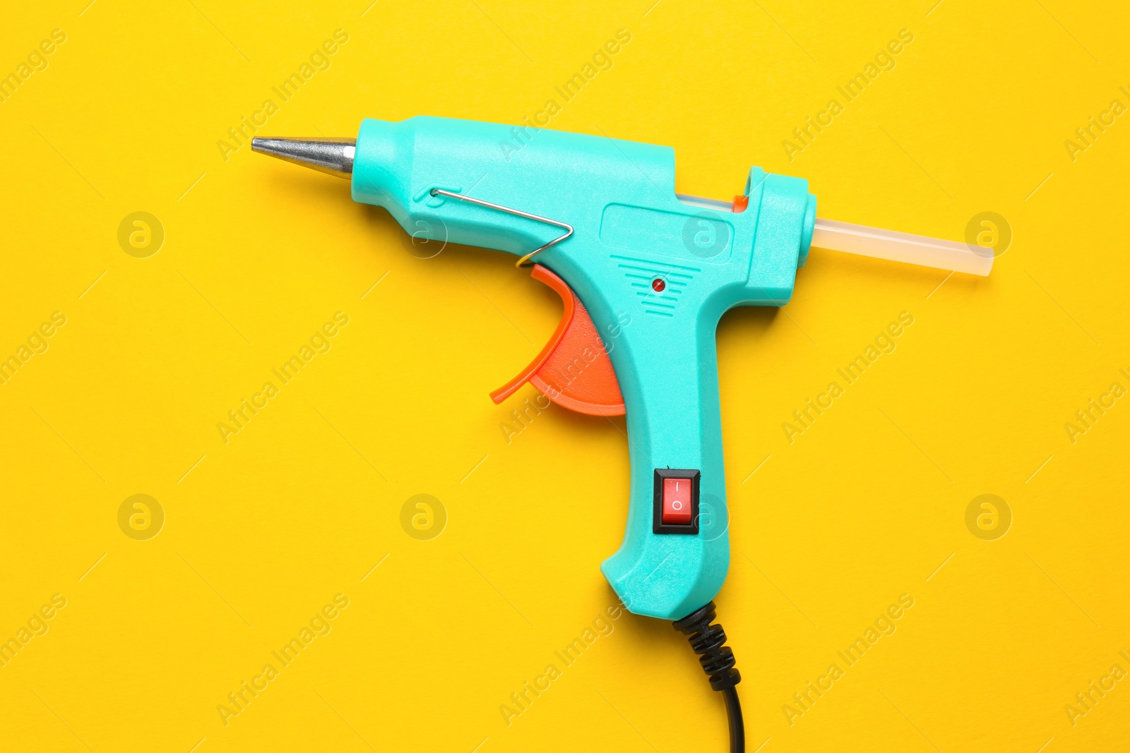 Photo of Turquoise glue gun with stick on yellow background, top view