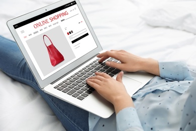 Woman shopping online using laptop on bed, closeup