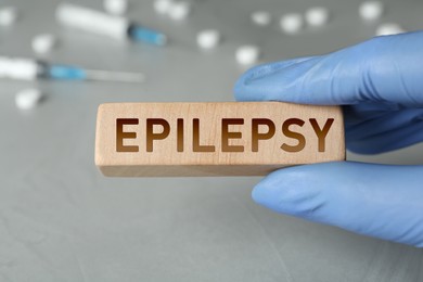 Photo of Doctor holding wooden block with word Epilepsy at grey table, closeup