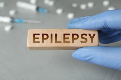 Doctor holding wooden block with word Epilepsy at grey table, closeup