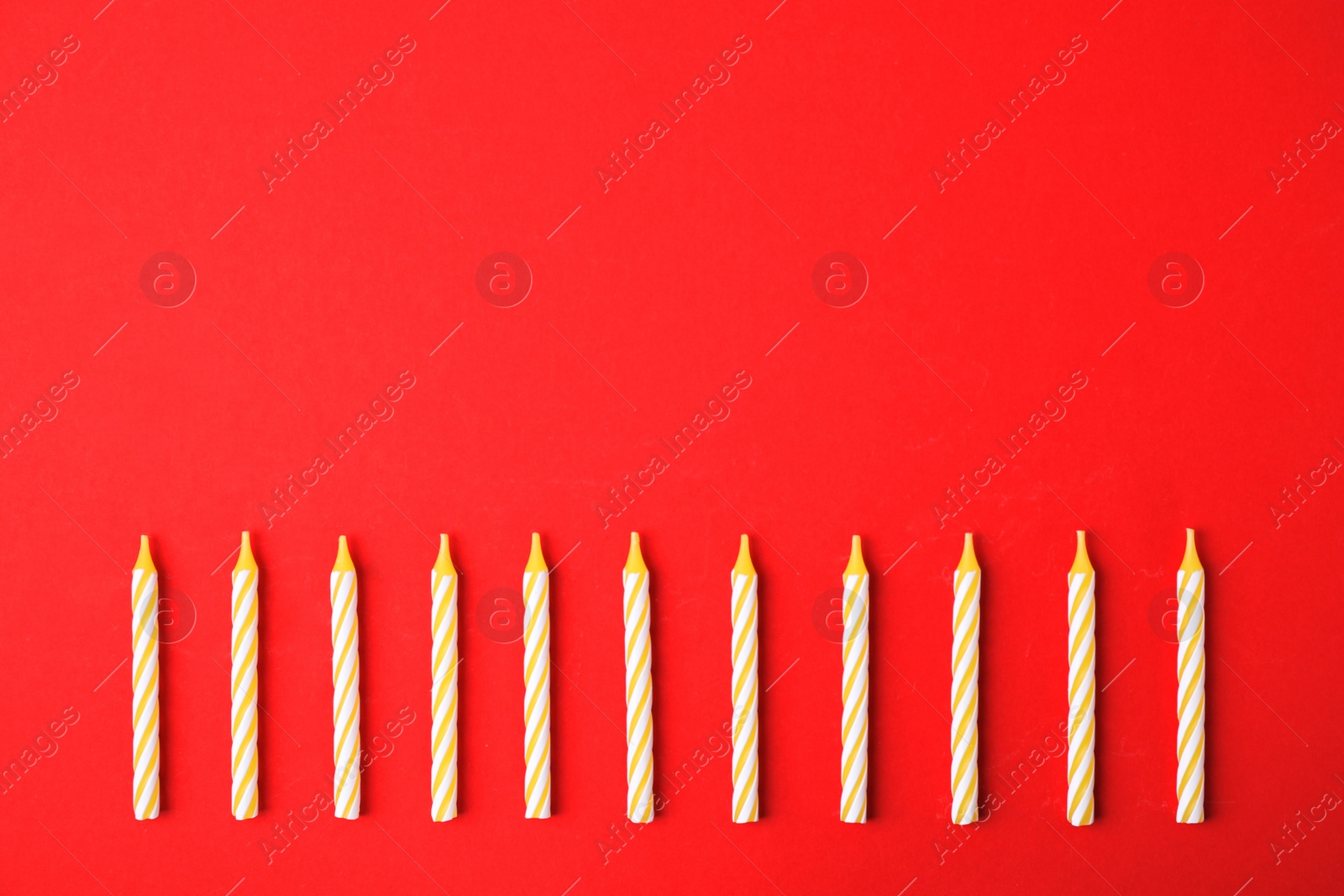 Photo of Yellow striped birthday candles on red background, top view with space for text