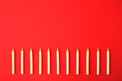 Yellow striped birthday candles on red background, top view with space for text