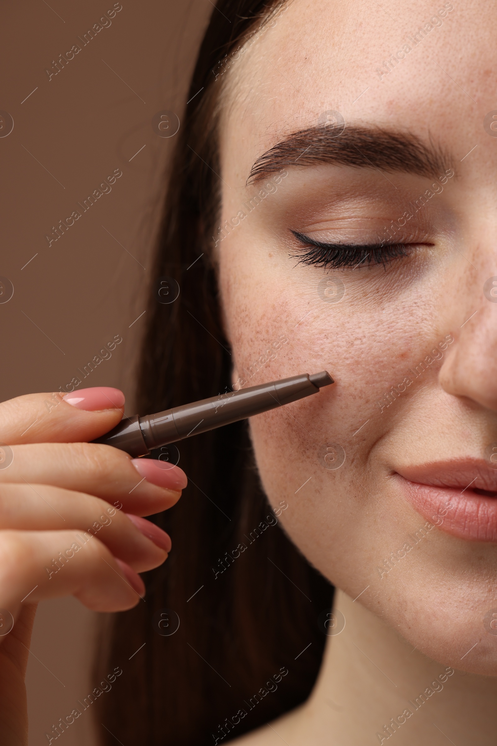 Photo of Beautiful woman drawing freckles with pen on brown background, closeup