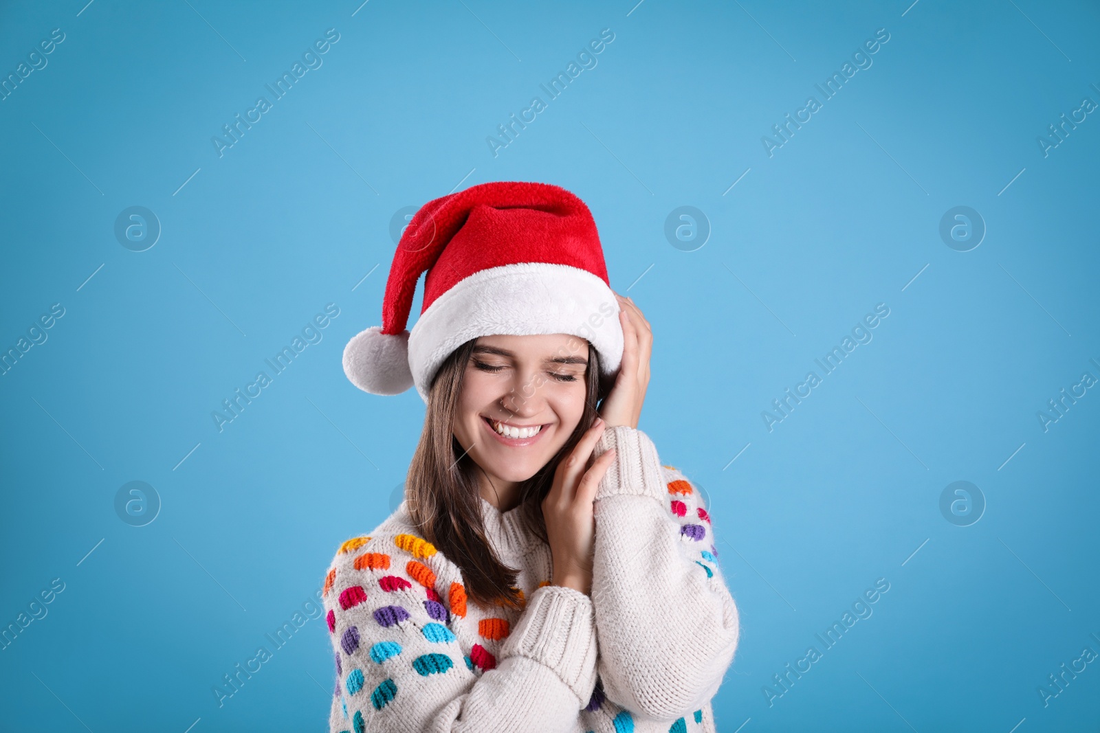 Photo of Pretty woman in Santa hat and festive sweater on light blue background