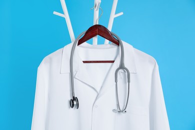 Photo of White medical uniform and stethoscope hanging on rack against light blue background