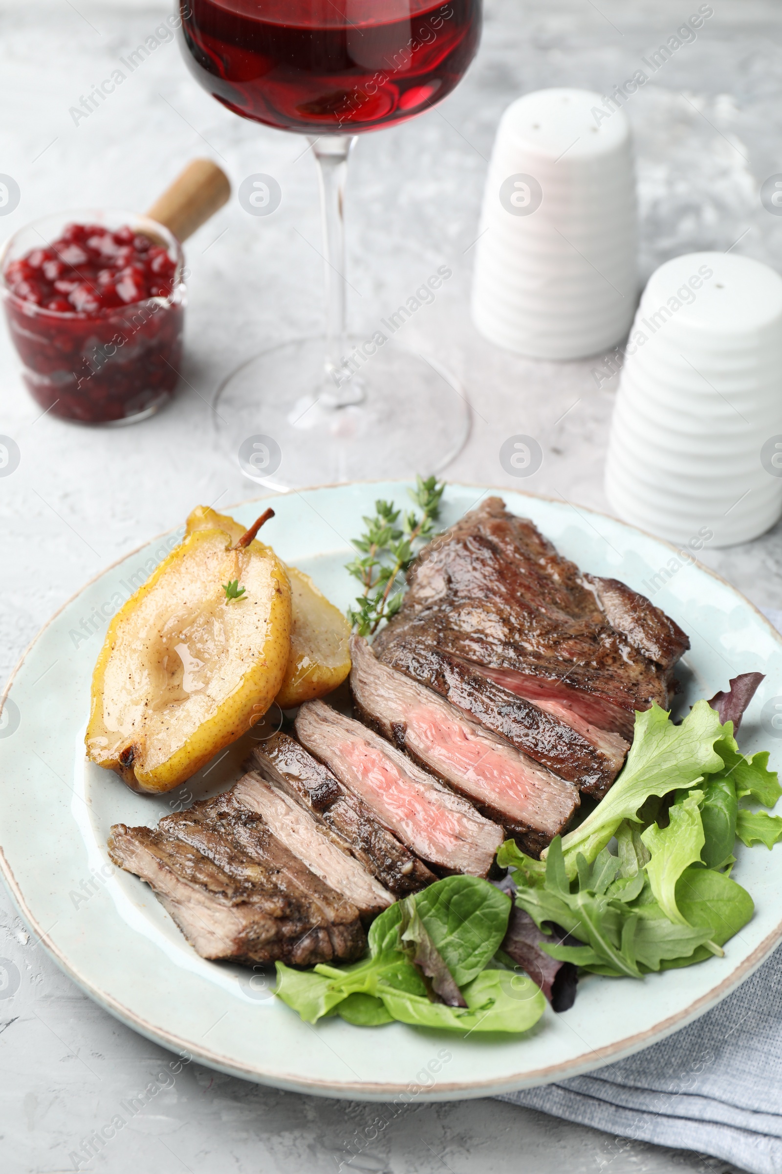 Photo of Delicious roasted beef meat, caramelized pear and greens served on light table