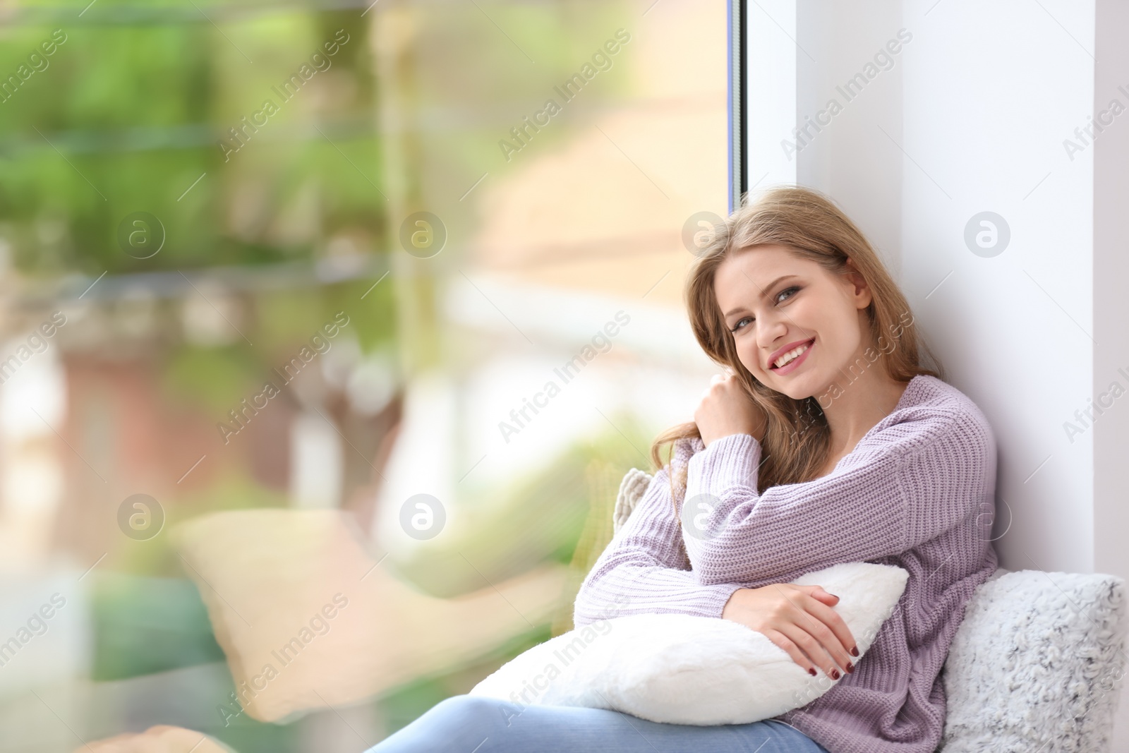 Photo of Young happy woman sitting near window at home