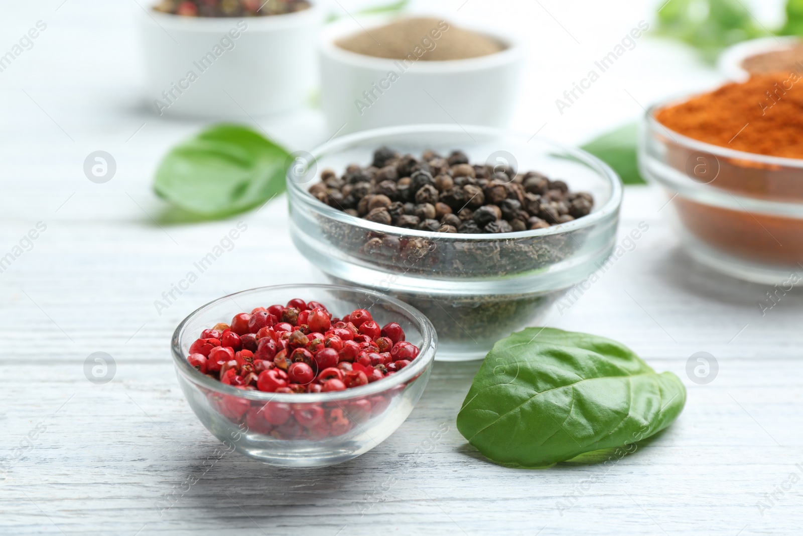 Photo of Glass bowls of red and black pepper corns on white wooden table