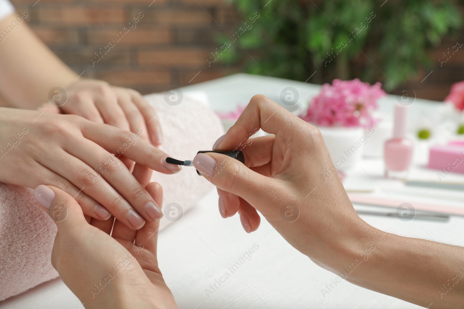 Photo of Manicurist applying polish on client's nails at table, closeup. Spa treatment