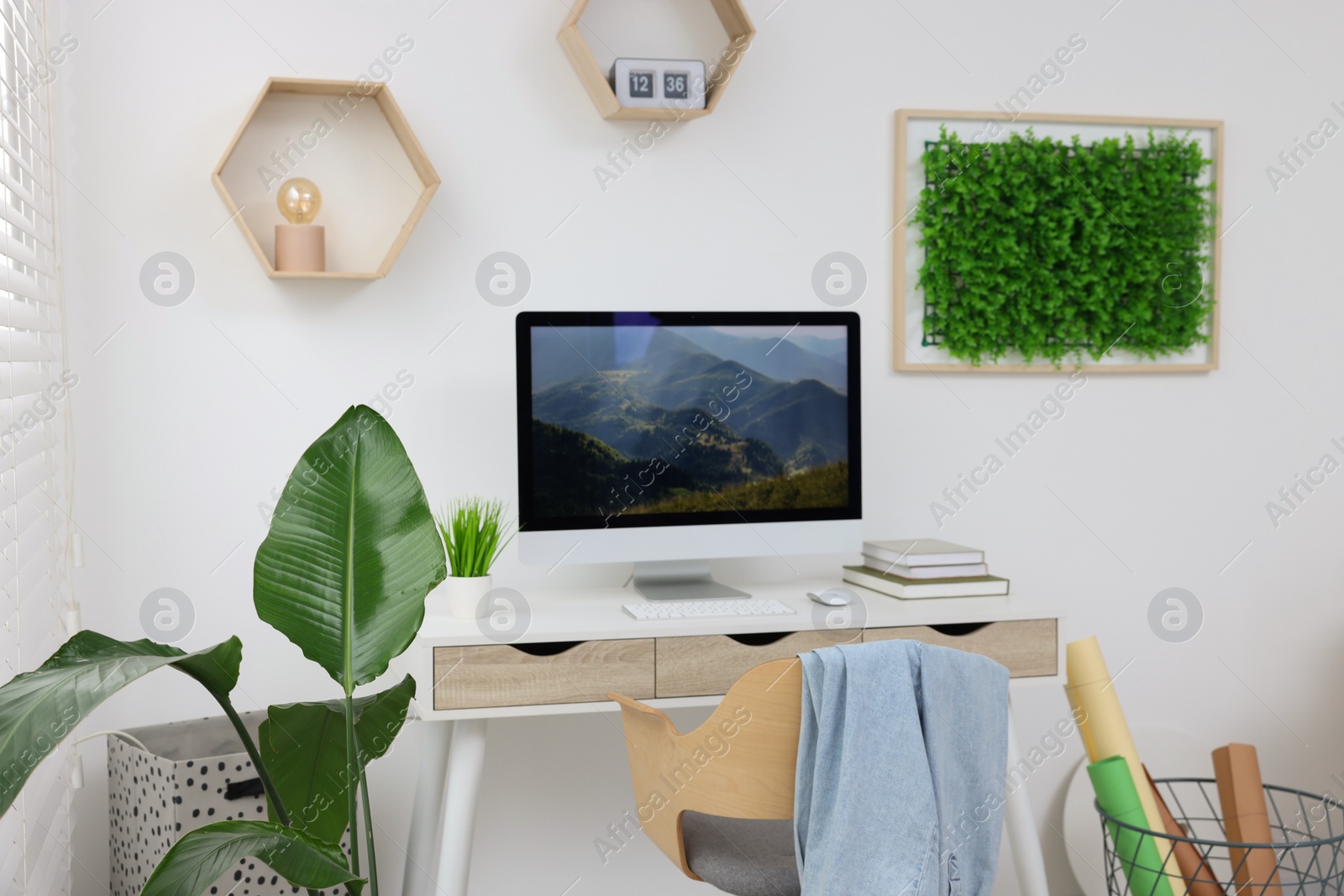 Photo of Green artificial plant wall panel and desk with computer in light room. Interior design