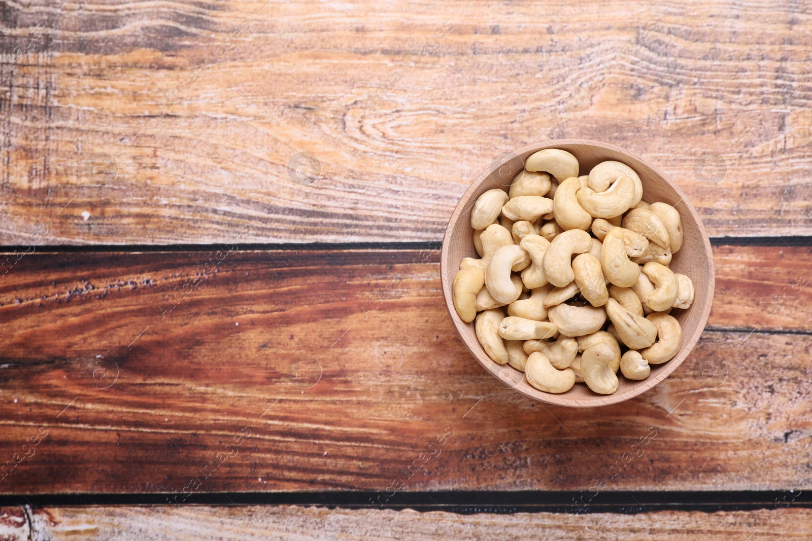 Photo of Tasty cashew nuts in bowl on wooden table, top view. Space for text