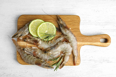 Photo of Fresh raw shrimps with lime slices and rosemary on white wooden table, top view