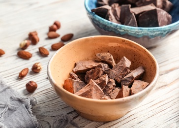 Bowl with pieces of delicious dark chocolate on wooden table