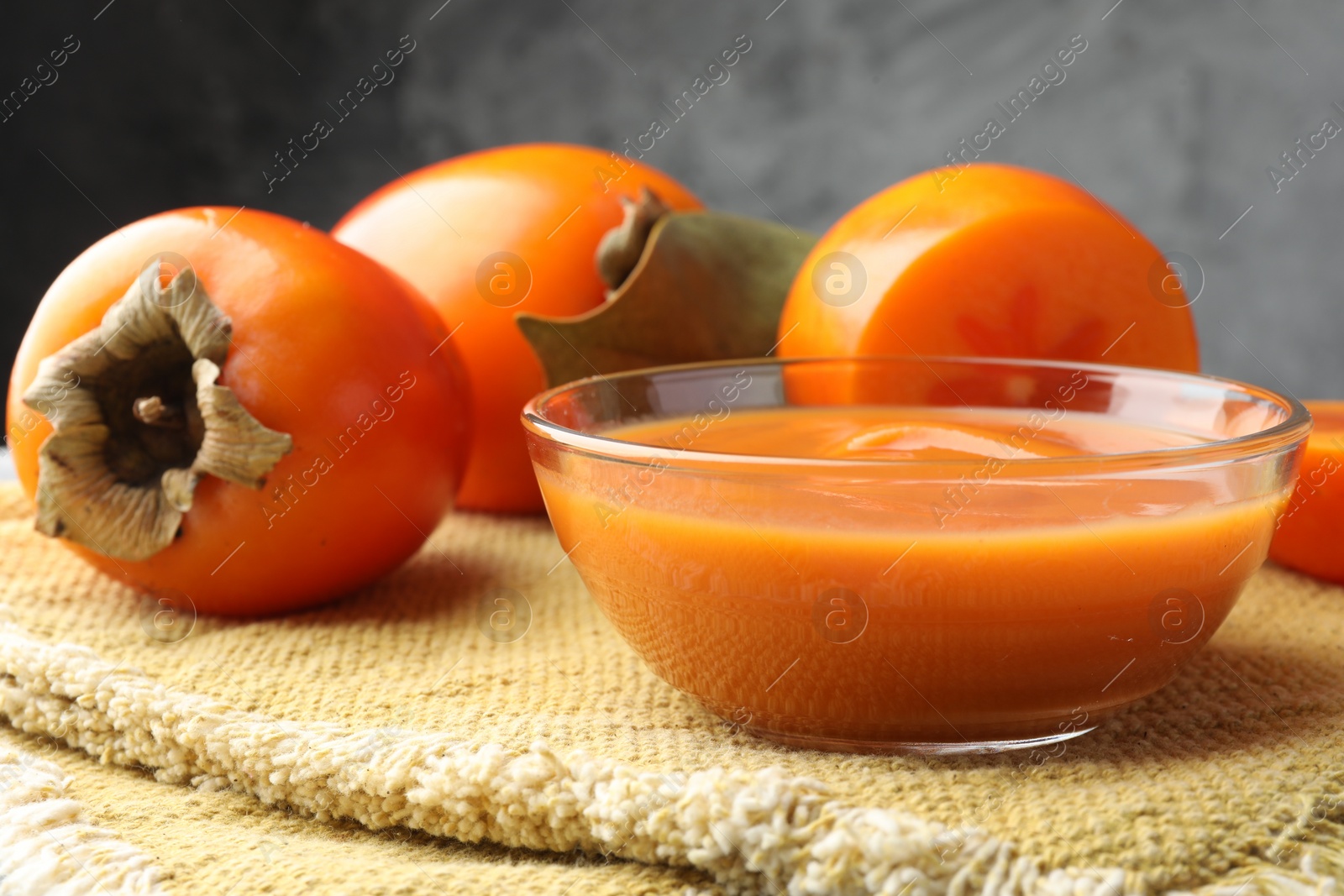 Photo of Delicious persimmon jam in glass bowl and fresh fruits on table, closeup