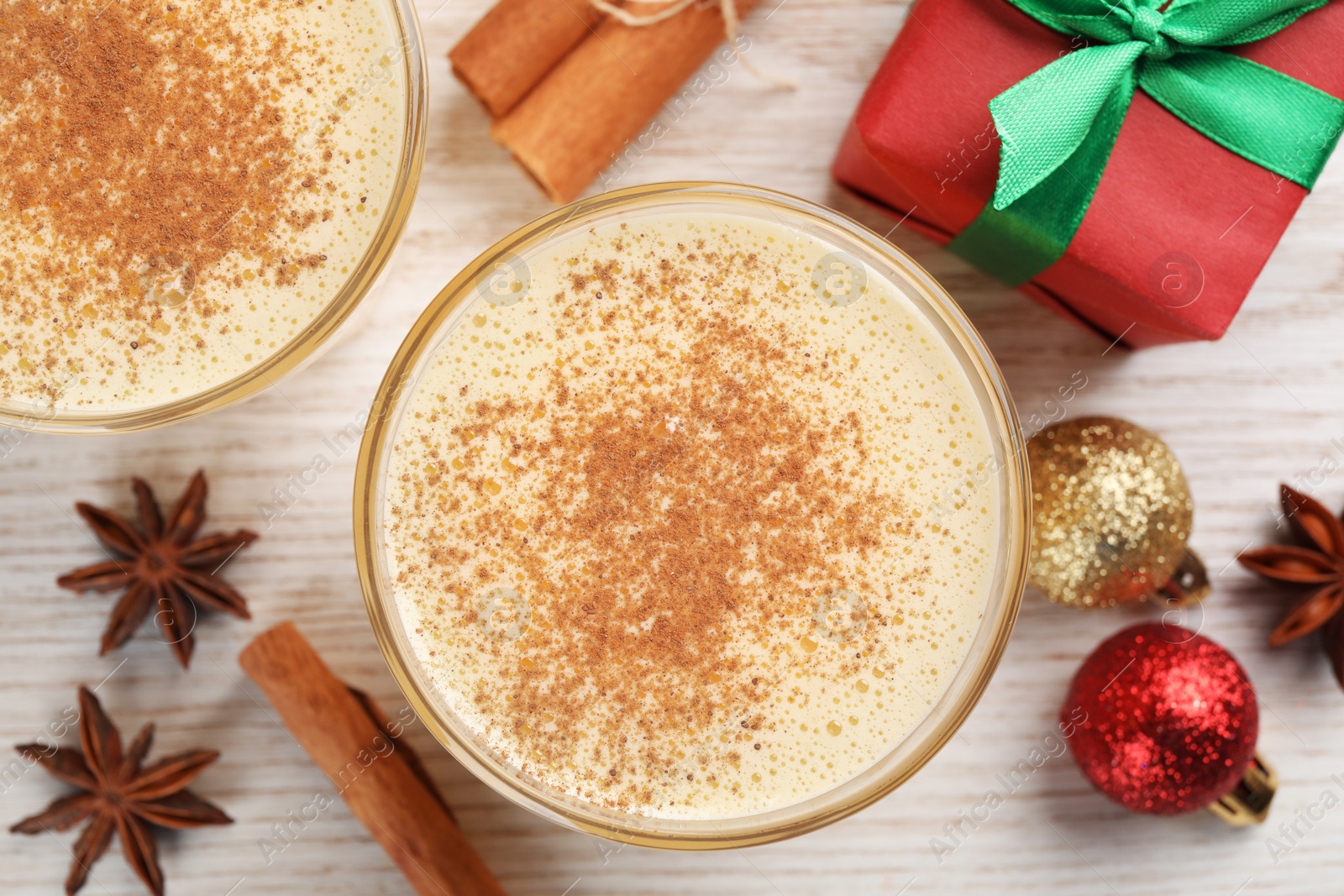 Photo of Tasty eggnog with cinnamon, anise stars and Christmas decorations on white wooden table, flat lay