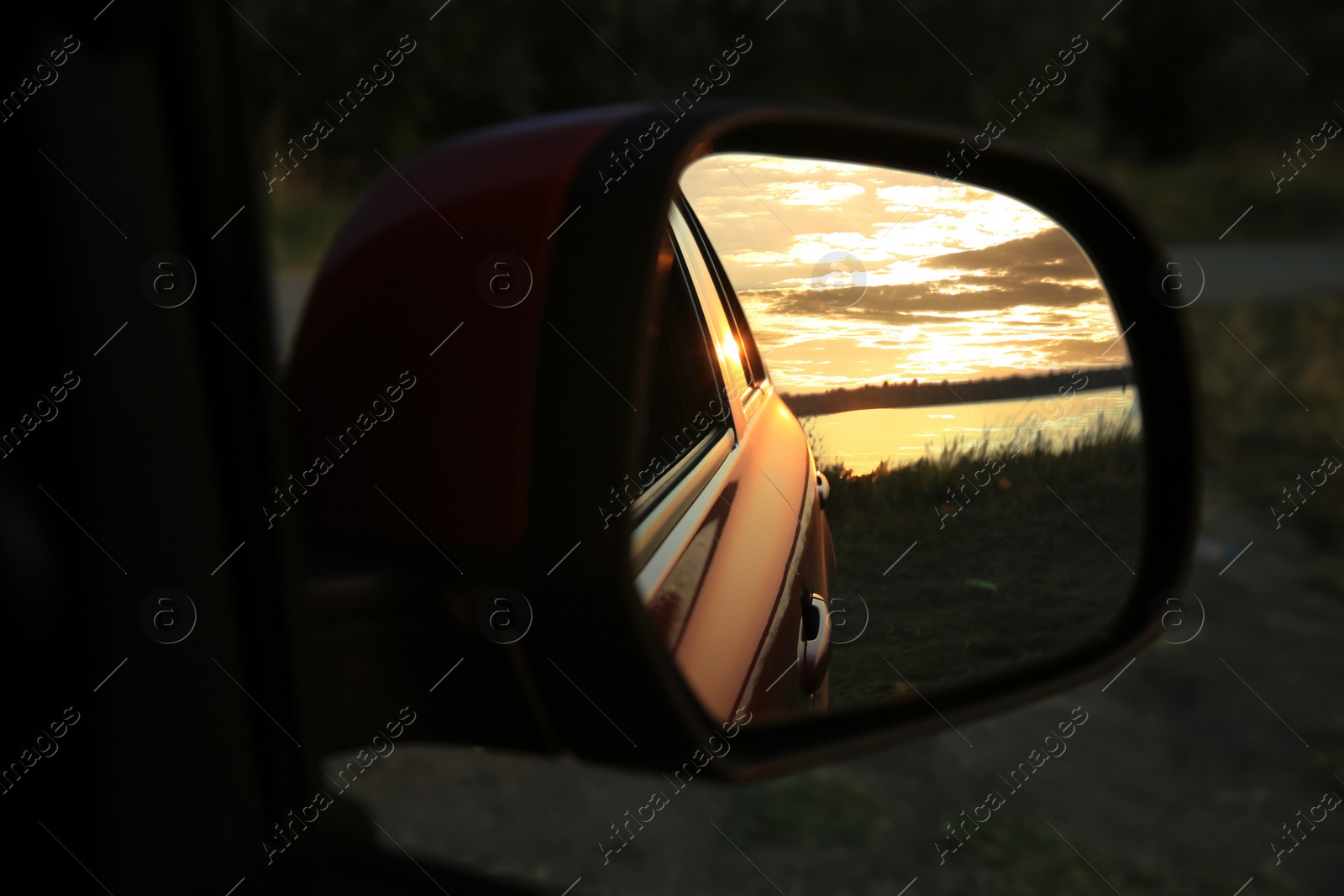 Photo of Reflection of landscape with beautiful sunset over calm river in car side view mirror, closeup