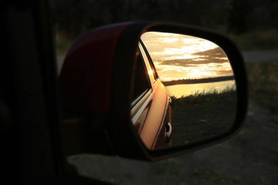 Photo of Reflection of landscape with beautiful sunset over calm river in car side view mirror, closeup